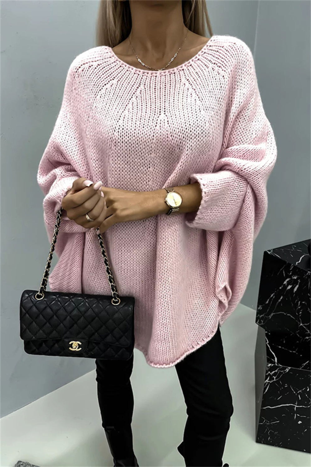 Blush pink knit sweater with relaxed fit and cape sleeves, featuring a wide neckline and textured knit pattern.