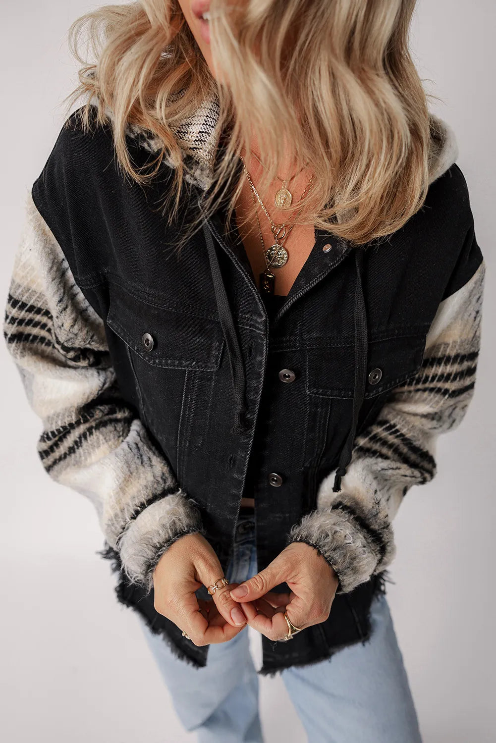 Black denim trucker jacket with plaid sleeves and hood, featuring frayed hem.