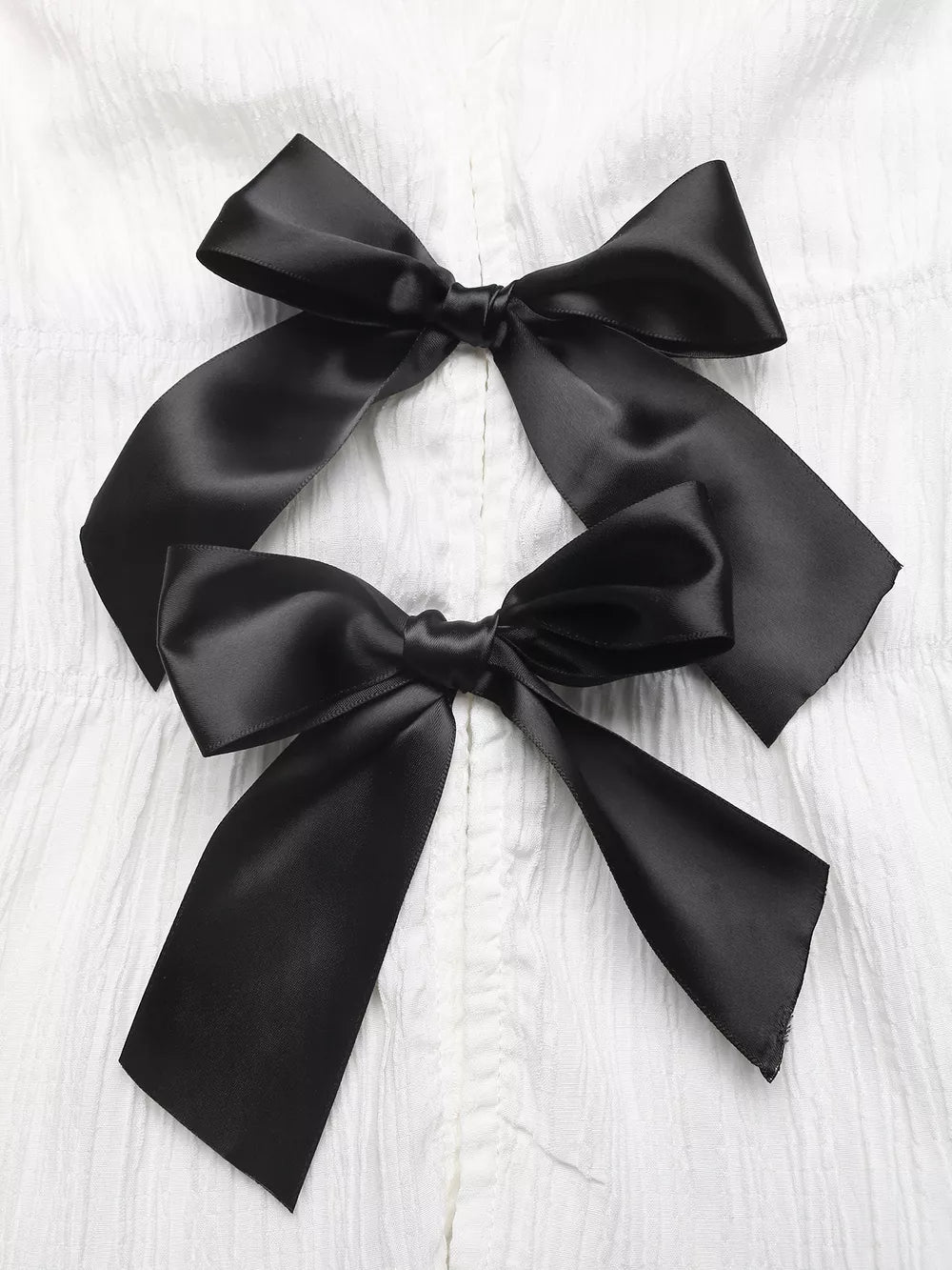 White maternity blouse with two black satin bow accents and cap sleeves.