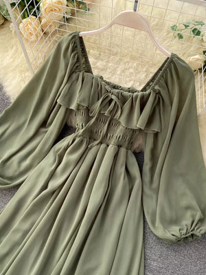 Green maternity dress with square neck, ruffled trim, smocked bodice, balloon sleeves, and tie detail.