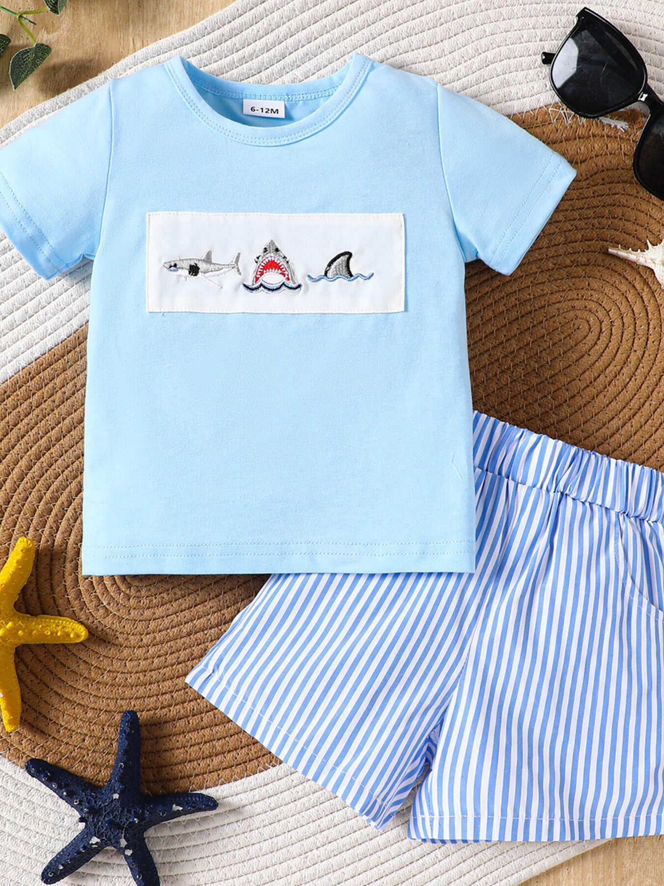 Baby blue cotton t-shirt with embroidered sharks and blue striped shorts.