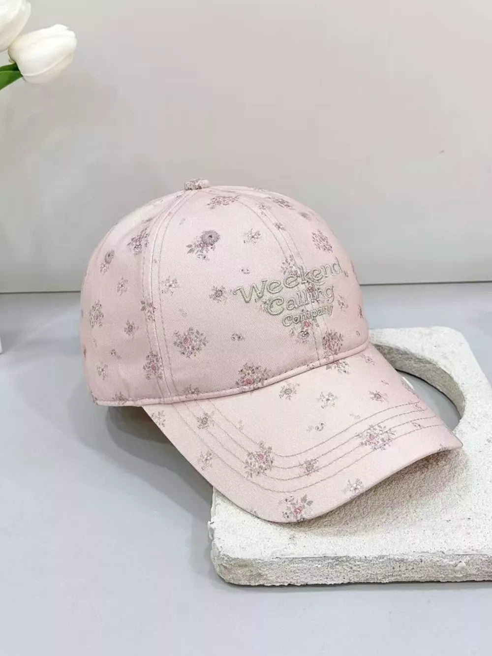 Embroidered floral baseball cap in blush pink cotton with "Weekend Calling Company" text.