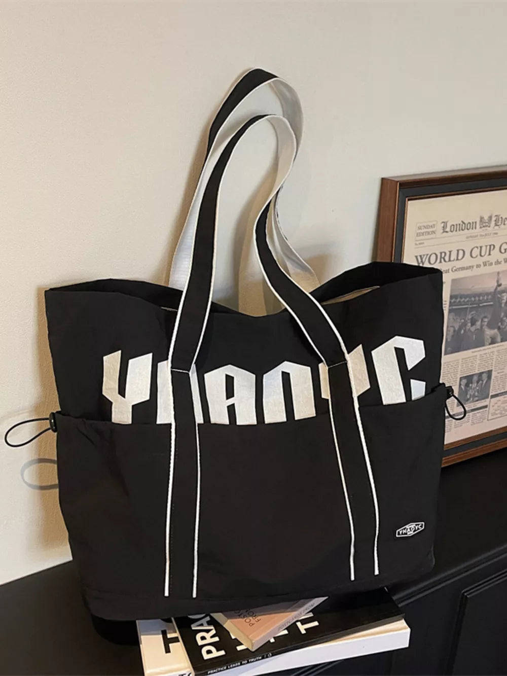 Black drawstring shoulder bag with bold white lettering and white trim.