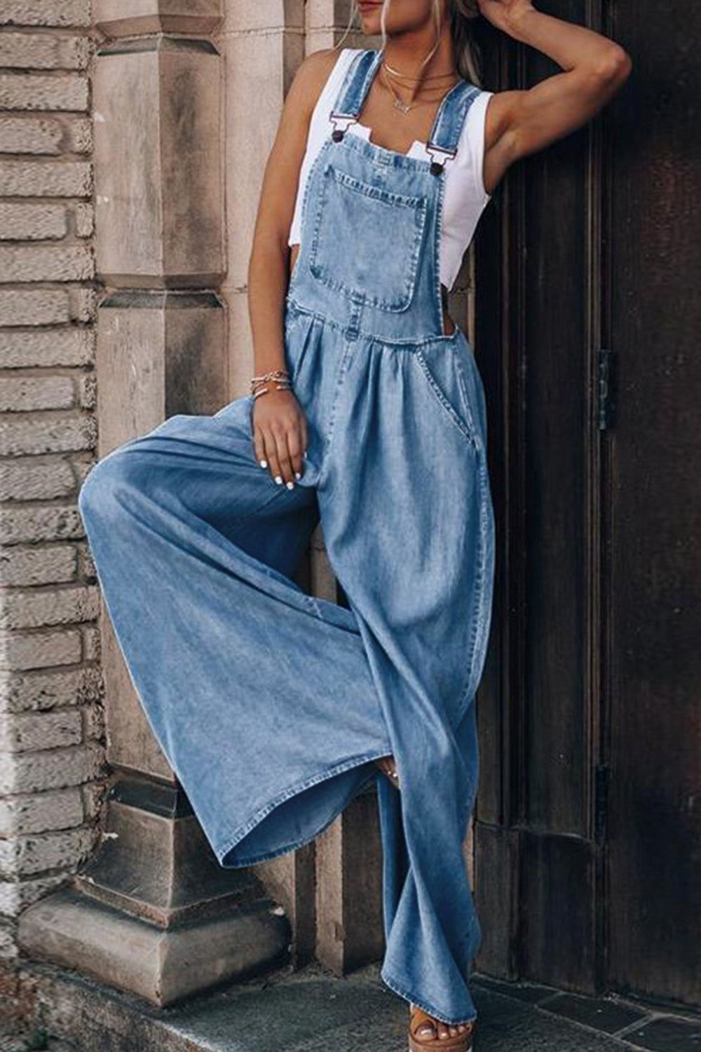 Distressed denim palazzo dungaree jumpsuit in light wash with wide legs and front bib pocket.