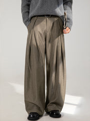Men's brown wide-leg trousers with pleats, styled with a grey sweater and black shoes.