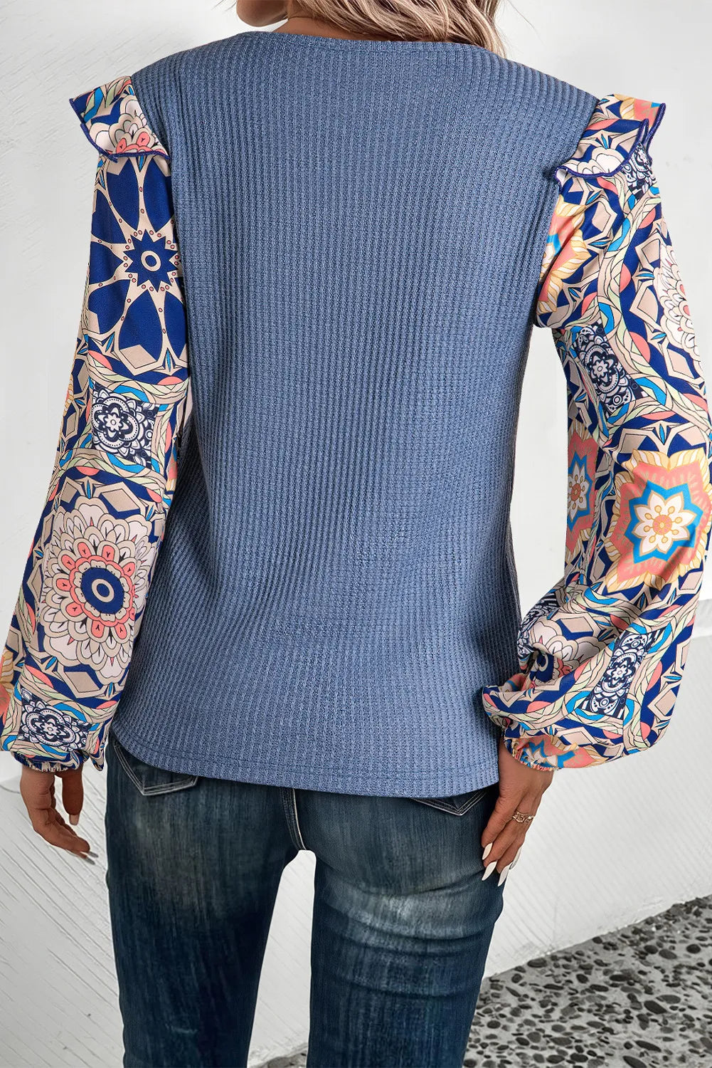 Dusty blue knit top with ruffled printed sleeves and a textured bodice.