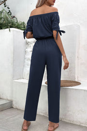Off-the-shoulder jumpsuit in dark blue with tie-sleeve detail and wide legs.