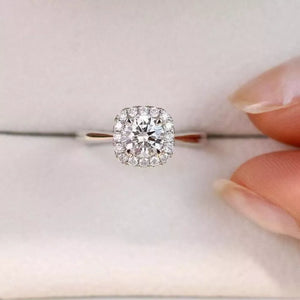 Elegant moissanite and sterling silver ring with cushion-cut center stone and halo of brilliant stones.