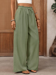 Crinkled wide-leg maternity pants in sage green with drawstring waist and pom-pom hem.