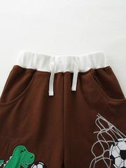 Brown cotton baby shorts with drawstring, white waistband, and dinosaur and soccer graphics.