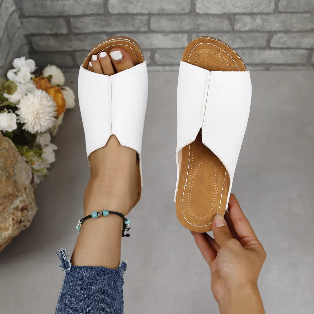White vegan leather asymmetrical slides with a pointed toe and tan sole.