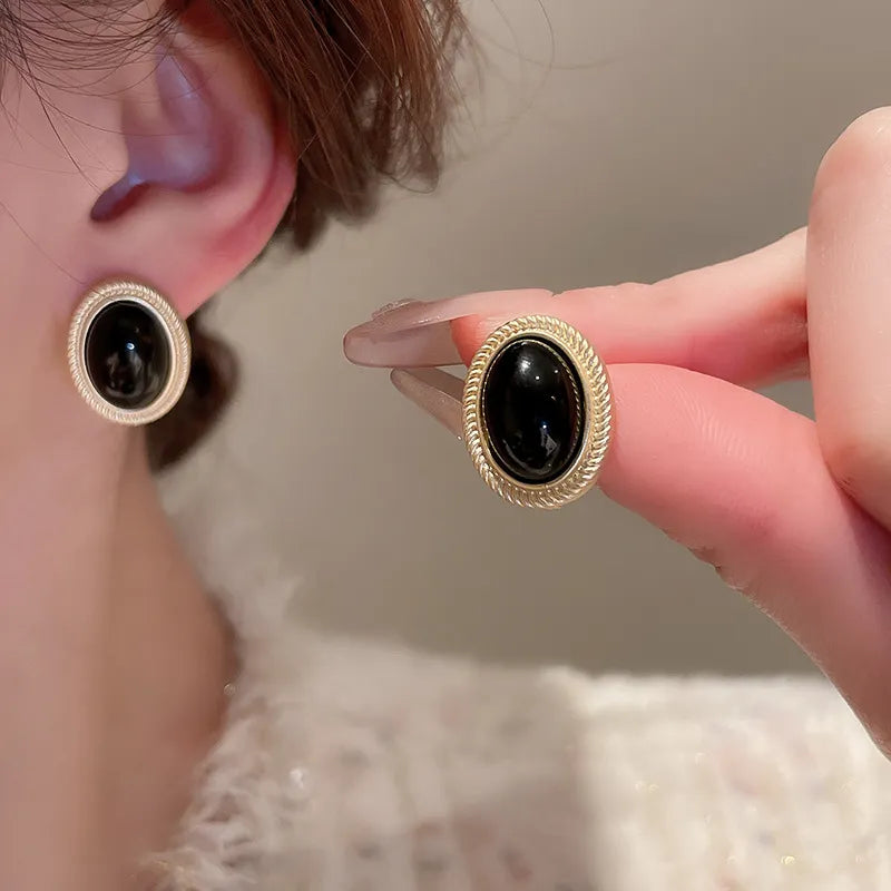 Gold oval stud earrings with black gemstone and textured rim