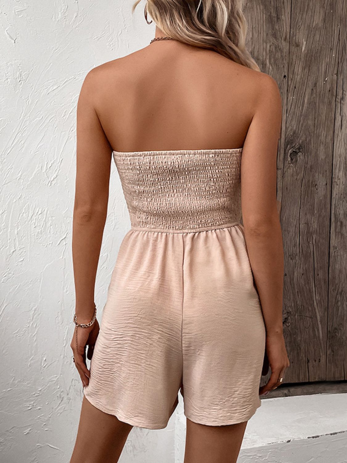 Tan smocked bodice strapless romper with tie-waist and textured shorts.