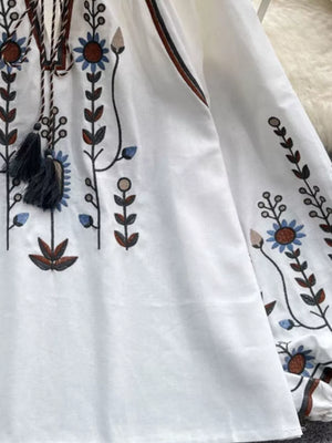 White embroidered tie neck blouse with billowy sleeves and floral details.