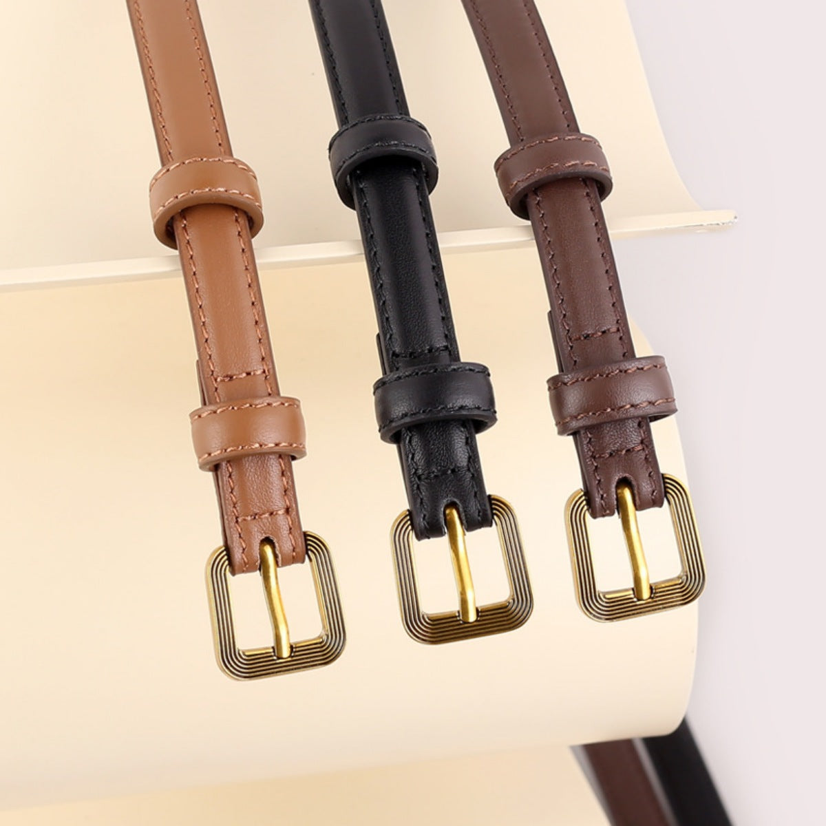 Sleek cowhide leather accent belts in brown, black, and caramel with antique brass buckles.