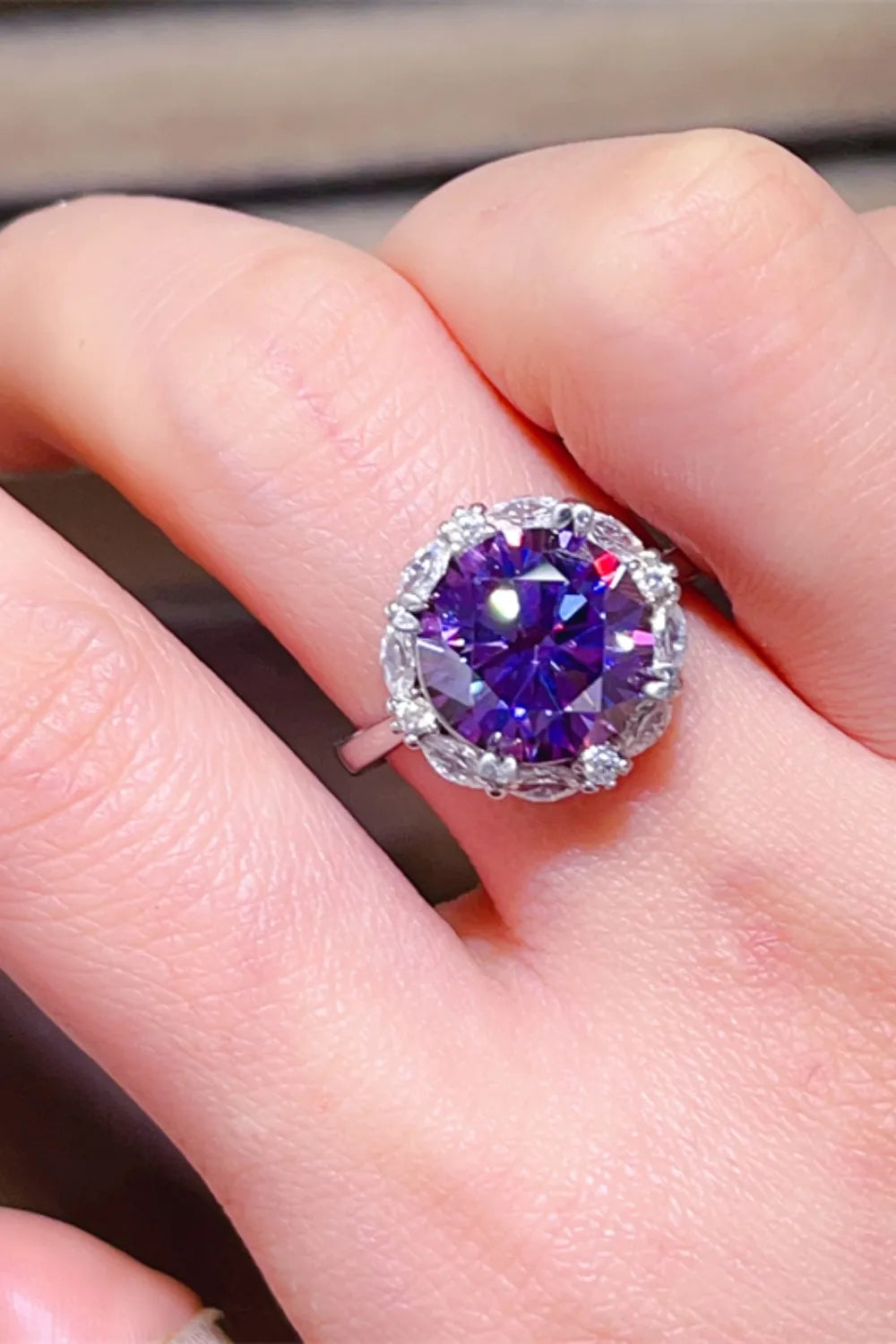 Amethyst halo cocktail ring in silver with a large faceted purple center stone surrounded by smaller clear stones.