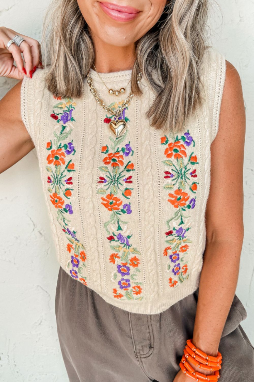 Beige cable knit vest with colorful floral embroidery and a crew neck.