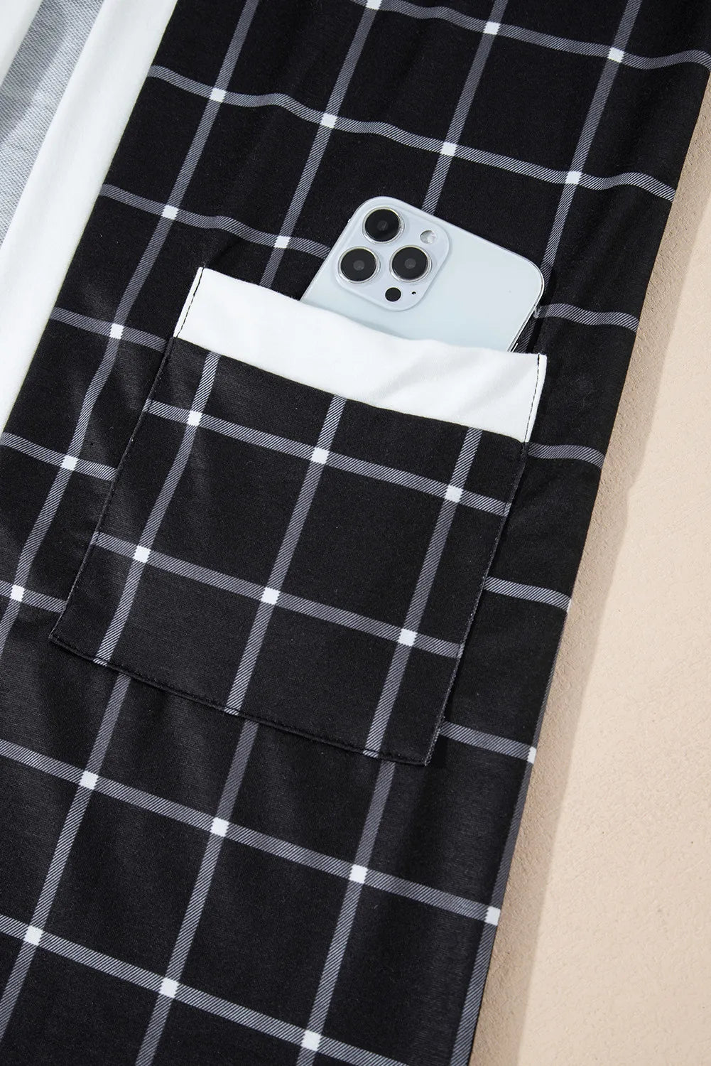 Black plaid duster cardigan with white trim and pocket detail, phone shown in pocket.