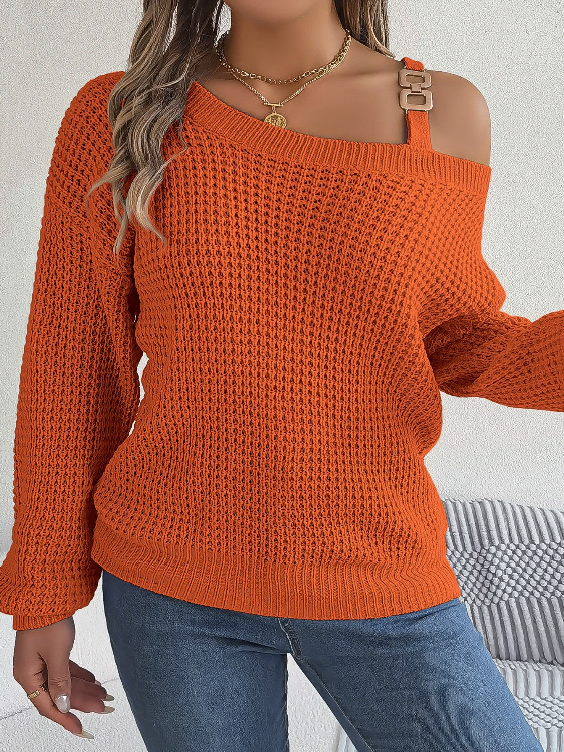 Orange one-shoulder knit sweater with buckle detail and waffle texture.