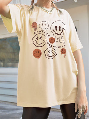 Tan oversized graphic tee with melting smiley faces and "Radiate Positivity" text.