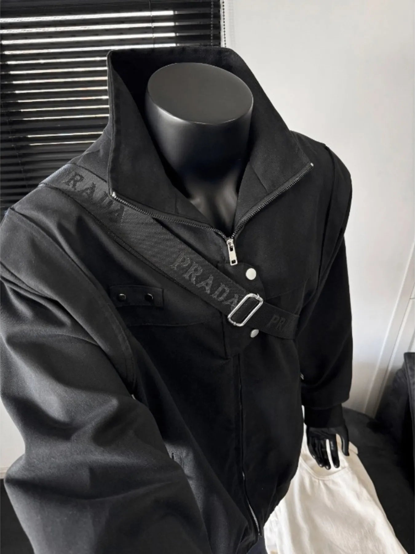 Black bomber jacket with zip closure, snap buttons, and a branded strap detail.