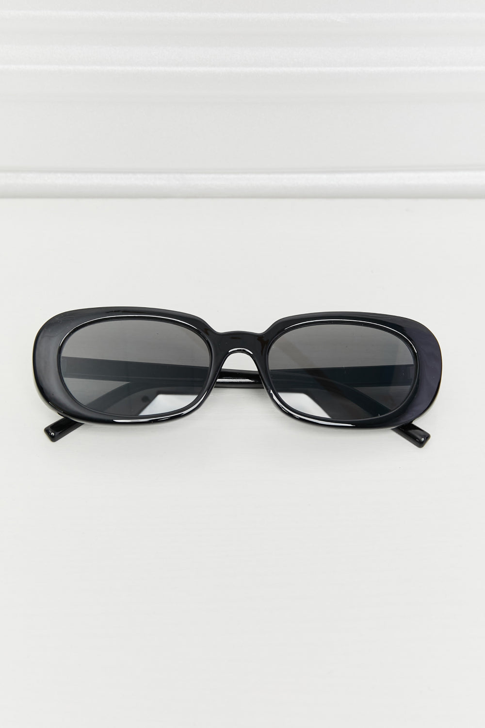 Black oval sunglasses with dark tinted lenses and a glossy finish.
