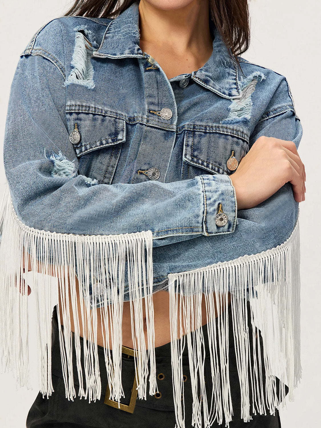 Distressed denim trucker jacket in medium wash with white fringe trim and distressed details.