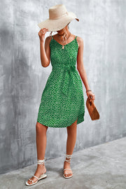 Green daisy print slip dress with tie waist and V-neck, styled with a straw hat and sandals.