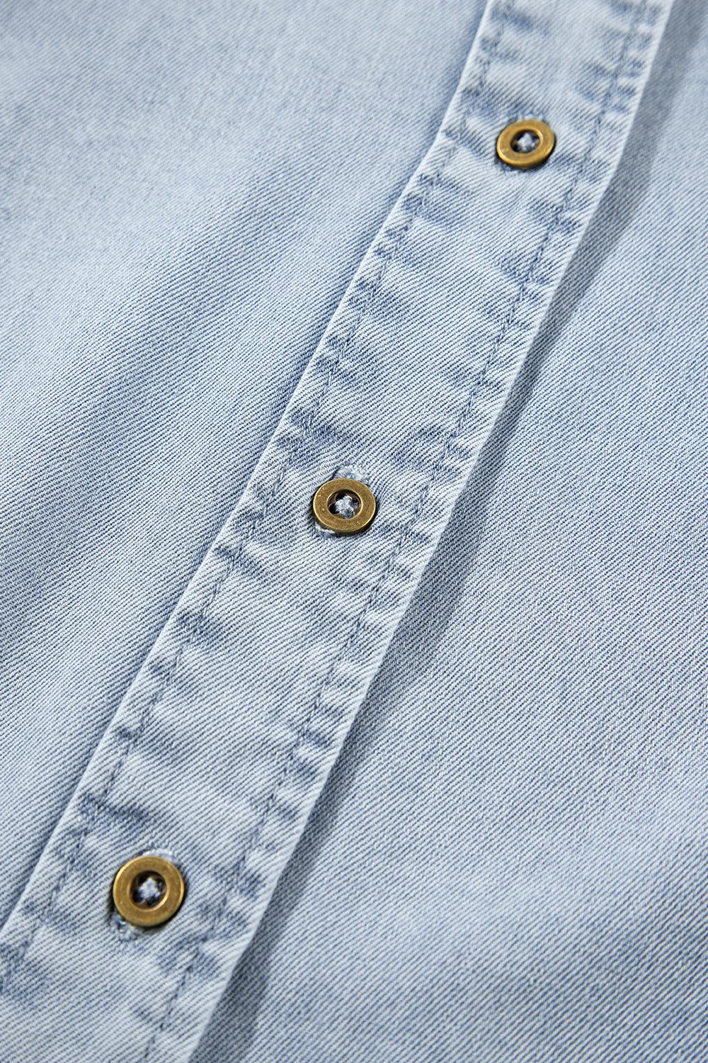 Light blue denim blouse with brass buttons and visible stitching detail.