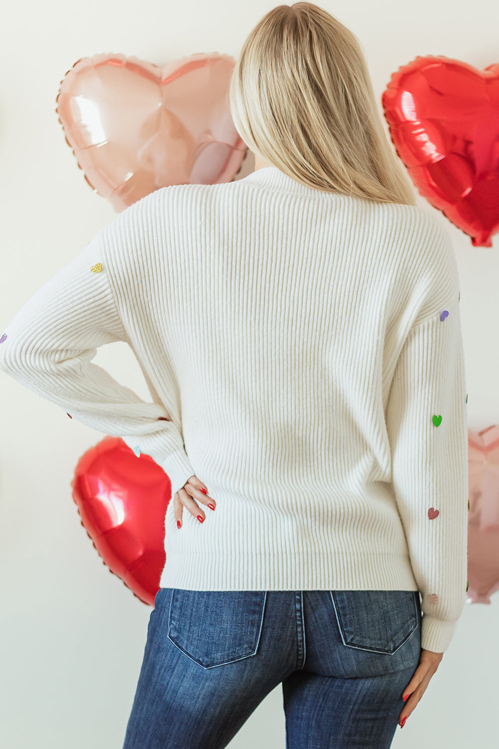 White ribbed knit sweater with colorful heart embellishments on sleeves.