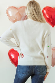 White ribbed knit sweater with colorful heart embellishments on sleeves.