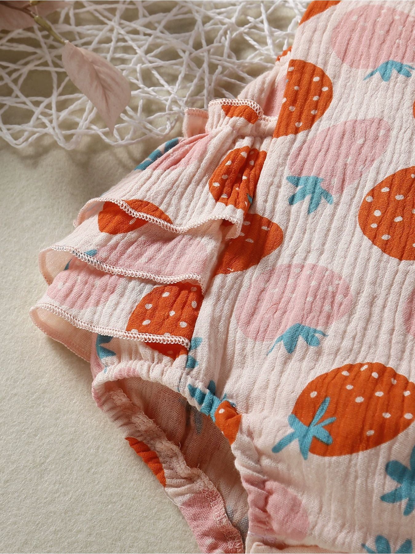 Baby bodysuit with tiered ruffle sleeves and a pink strawberry print on textured fabric.