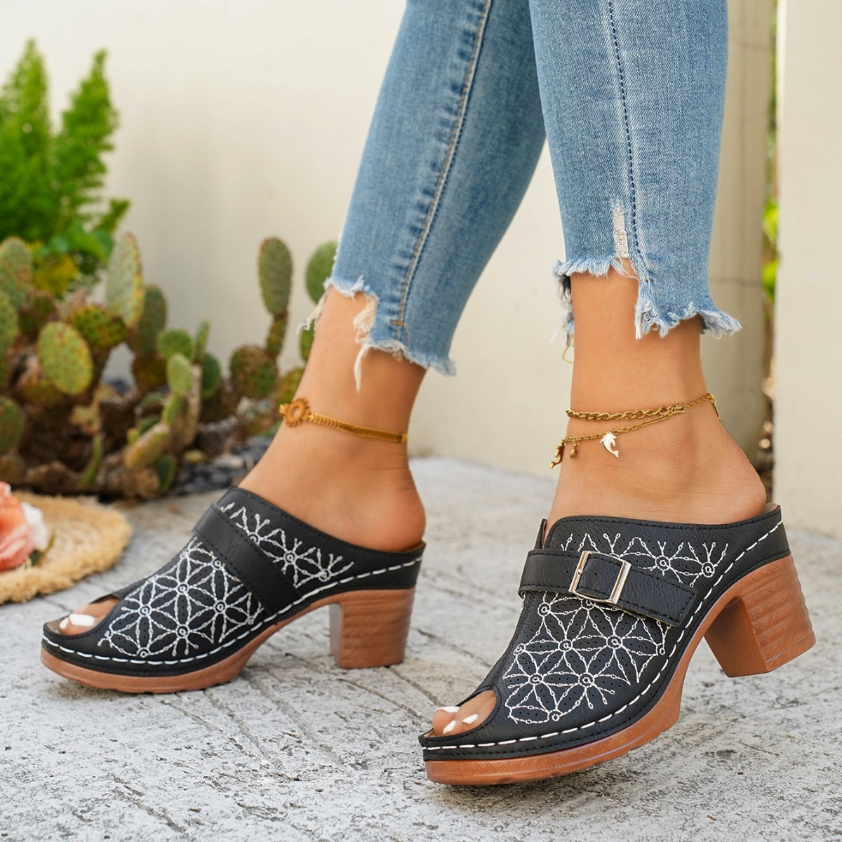 Black block heel sandals with white embroidery and buckle detail.