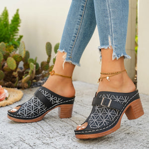 Black block heel sandals with white embroidery and buckle detail.