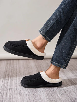 Black suede shearling-lined moccasin slides with contrast stitching and a small tan accent.