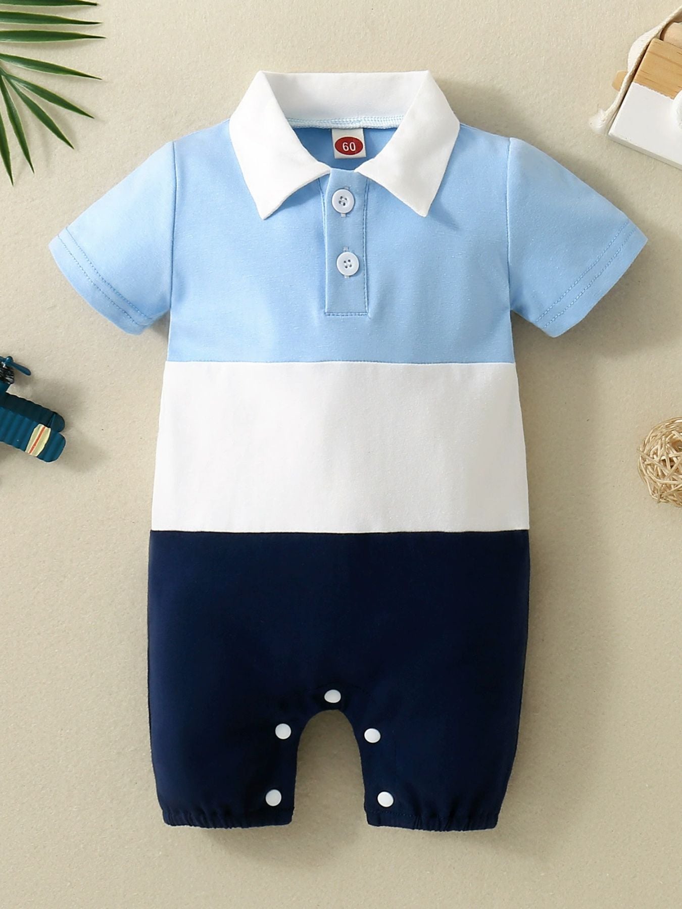 Baby color block polo one-piece in sky blue, white, and navy cotton with short sleeves and snap closure.