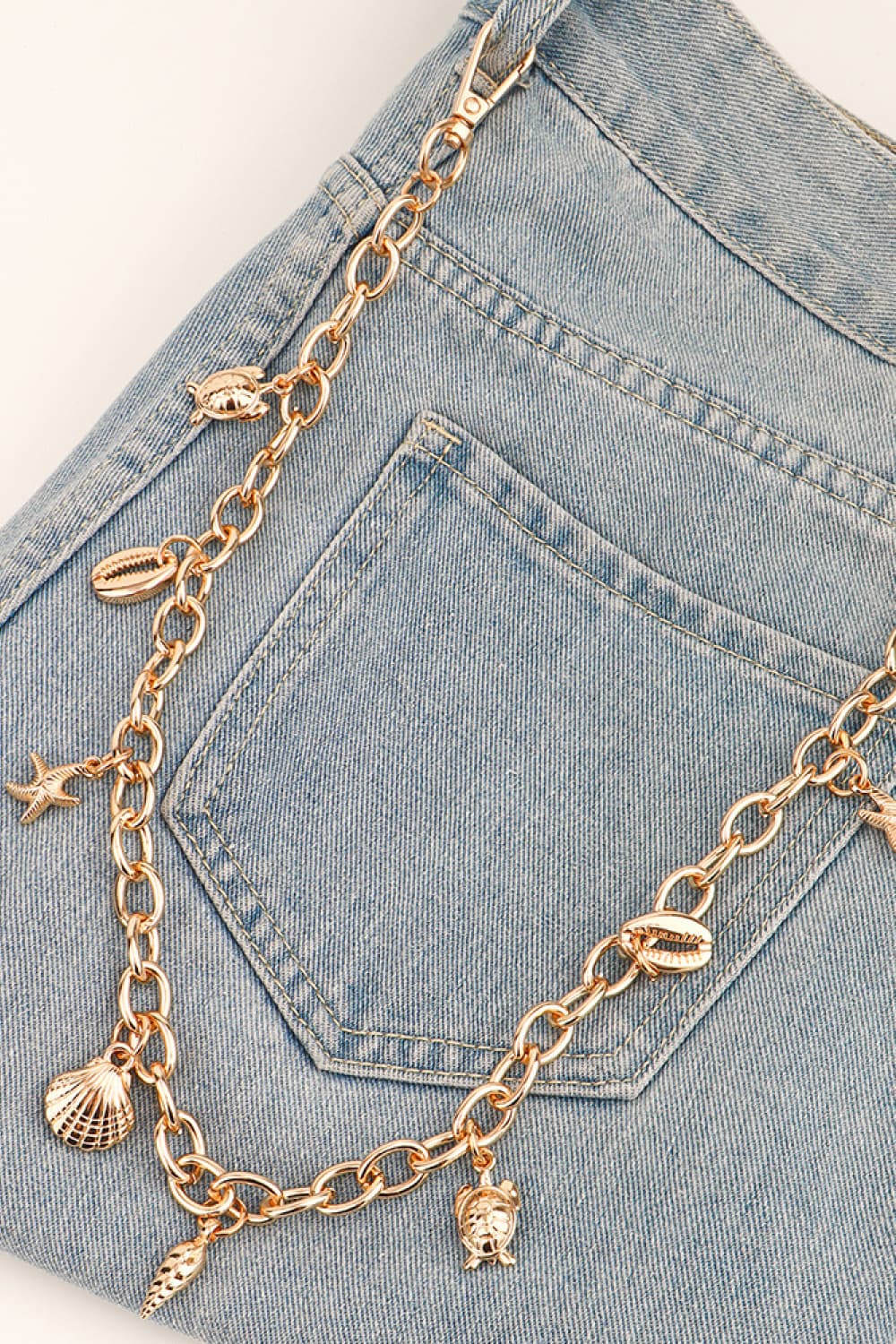 Gold chain belt with seashell, starfish, and turtle charms styled on denim.
