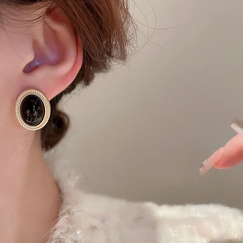 Gold oval stud earrings with black gemstone and textured border