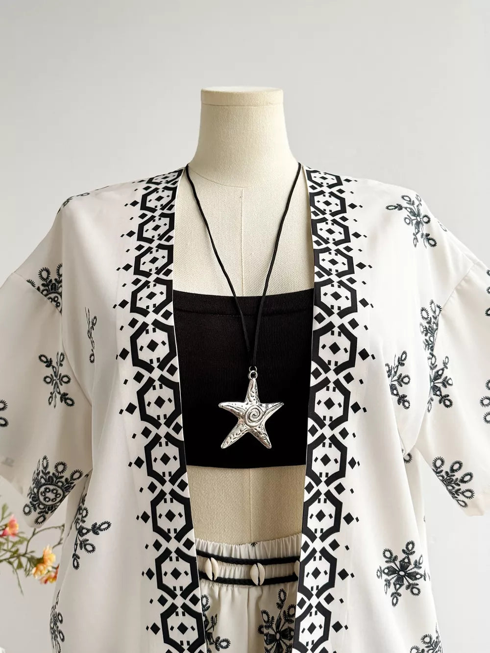 White polyester kimono jacket with black geometric and floral print, worn over a black crop top and shorts.
