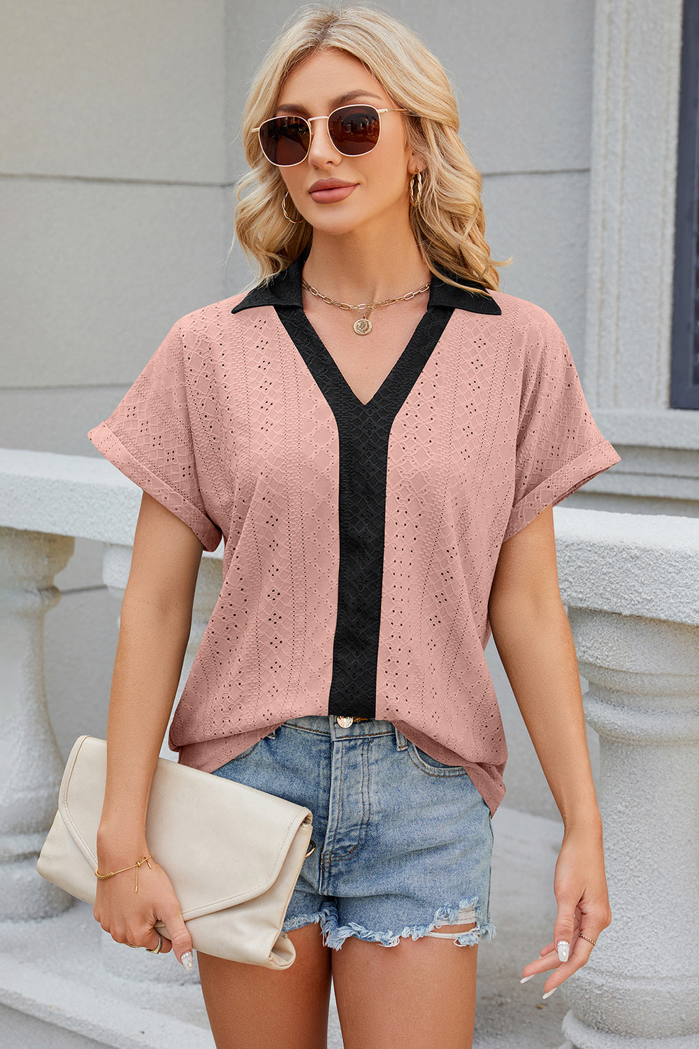 Blush pink perforated polo top with black V-neck detail and short sleeves.