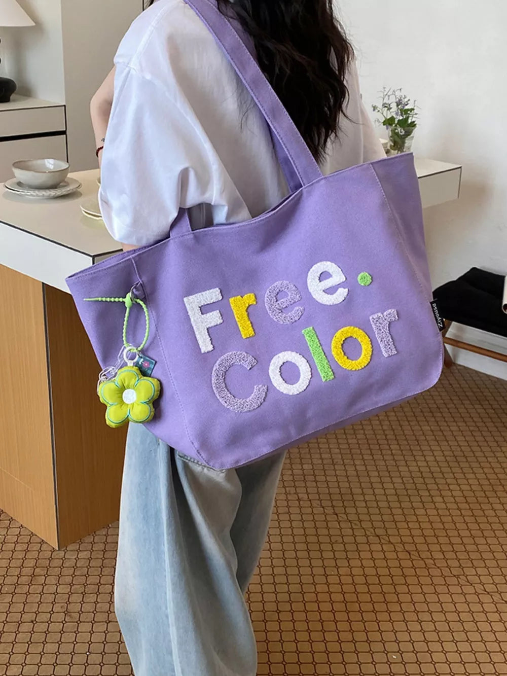 Lavender canvas shoulder bag with embroidered "Free. Color" text and flower charm