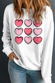 White crewneck sweatshirt with a grid of nine pink and red heart graphics.