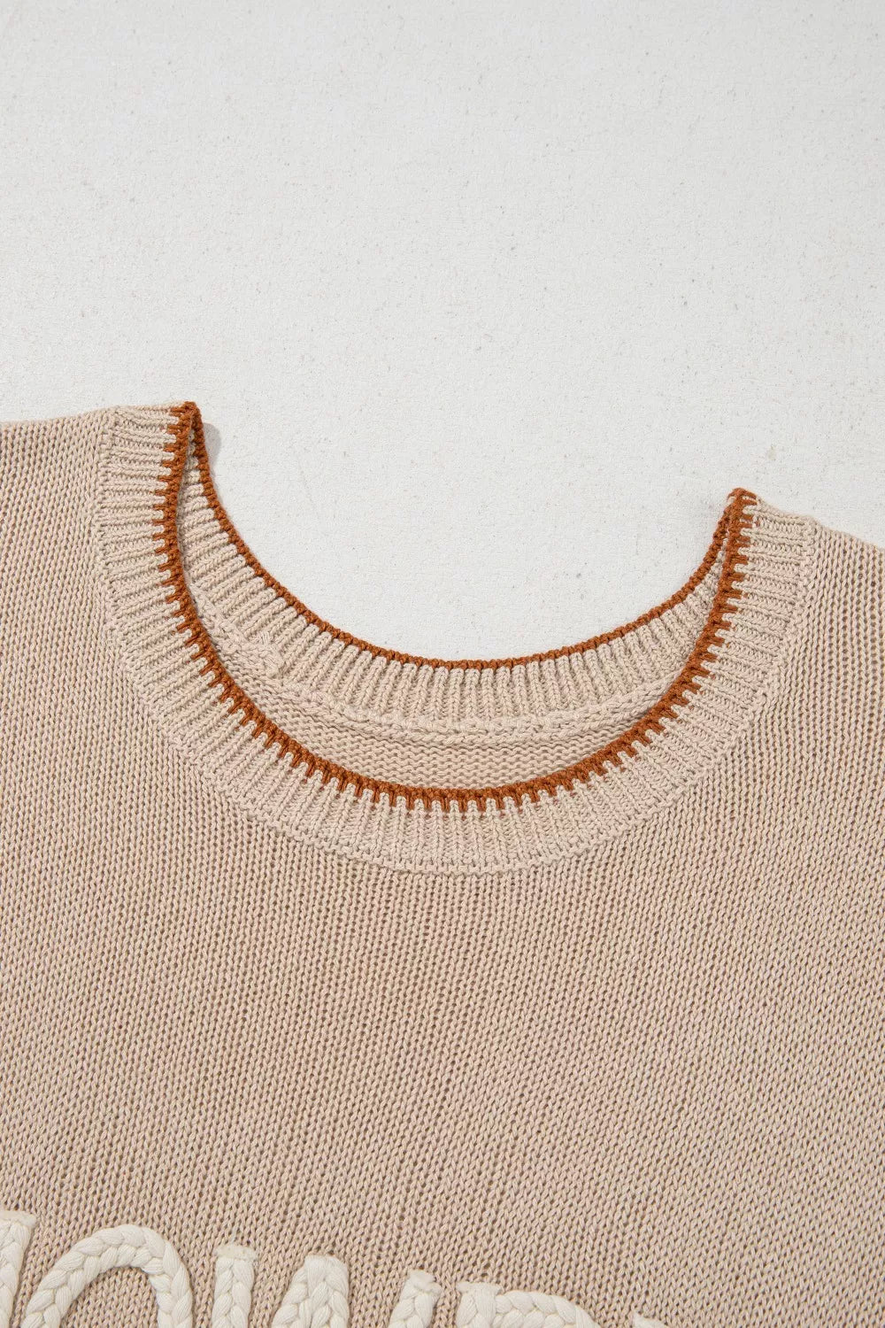 Beige knit sweater vest with contrast trim and textured lettering detail.