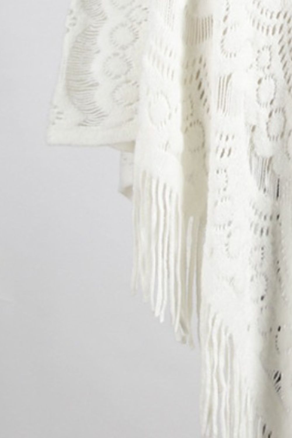 White crochet poncho with open knit pattern and fringe detail