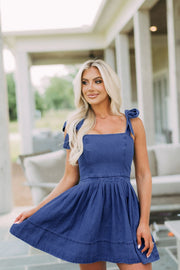 Denim tie-strap fit-and-flare mini dress in dark blue with a square neckline and pleated skirt.