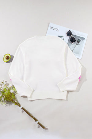 White knit sweater with embroidered pink blooms on the sleeves and a crew neckline.