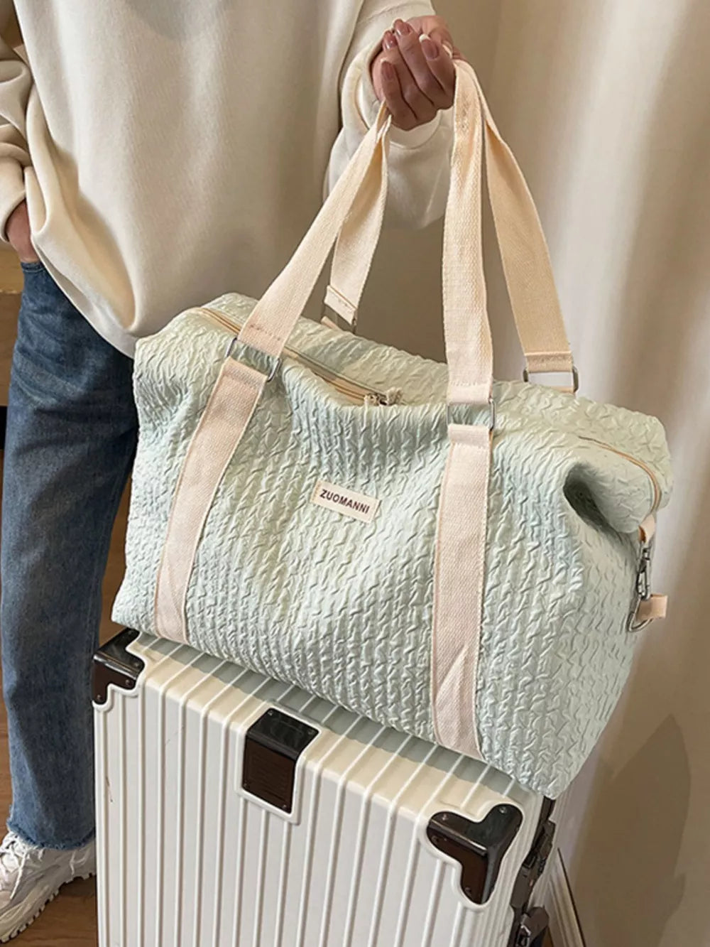 Textured travel bag with cream straps and detachable pouch, shown on a suitcase.