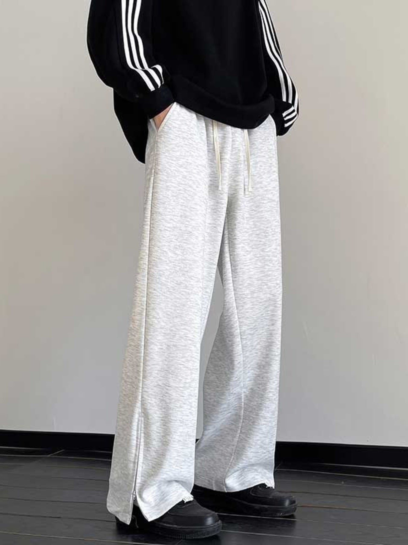 Men's light gray relaxed fit sweatpants with drawstring and zippered leg openings.