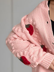 Pink knit cardigan with strawberry patches and textured sleeves.