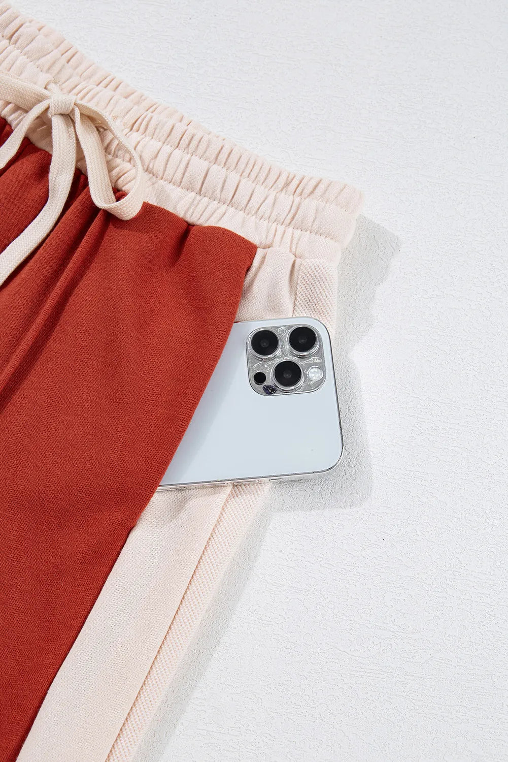 Terracotta and cream panel track pants with drawstring waist and phone pocket detail.